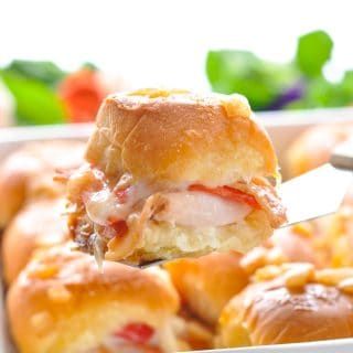 a close up of a sandwich being held by a person's hand in a white casserole dish