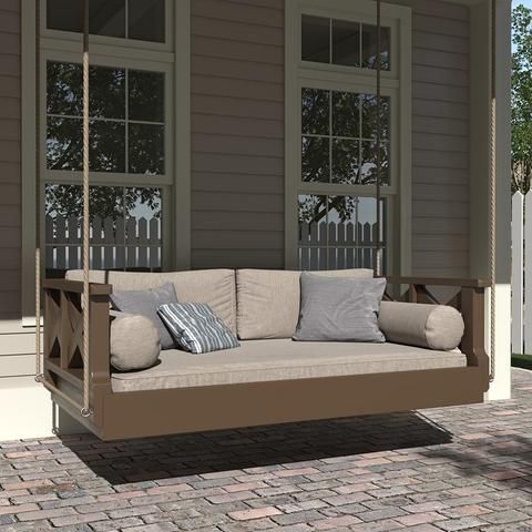 a porch swing with pillows on it sitting in front of a brick walkway and two windows