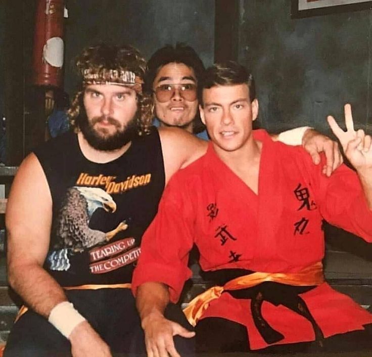 three men sitting on a bench posing for a photo with their hands in the air