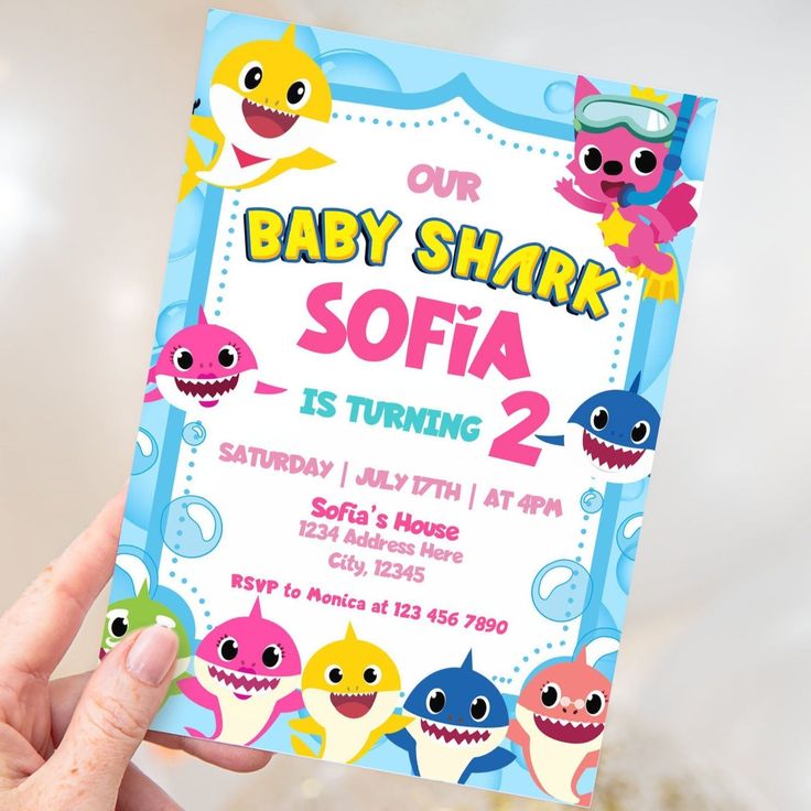 a person holding up a baby shark birthday party card in front of a white background