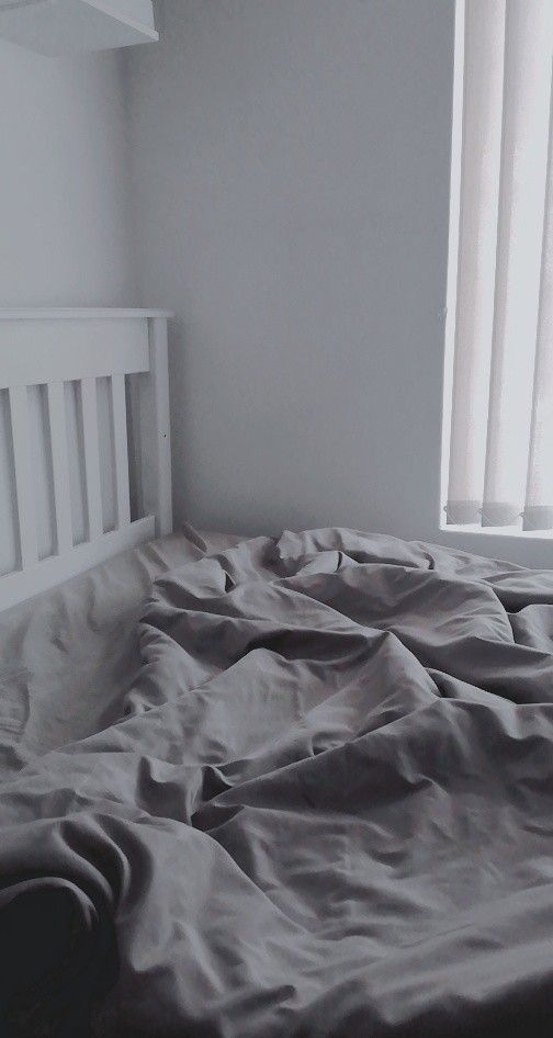 an unmade bed in a white room with a window behind it and sheets on the bed