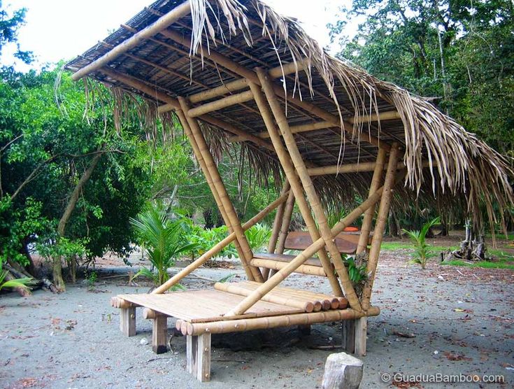 a wooden bench sitting under a thatched roof in a park area next to trees