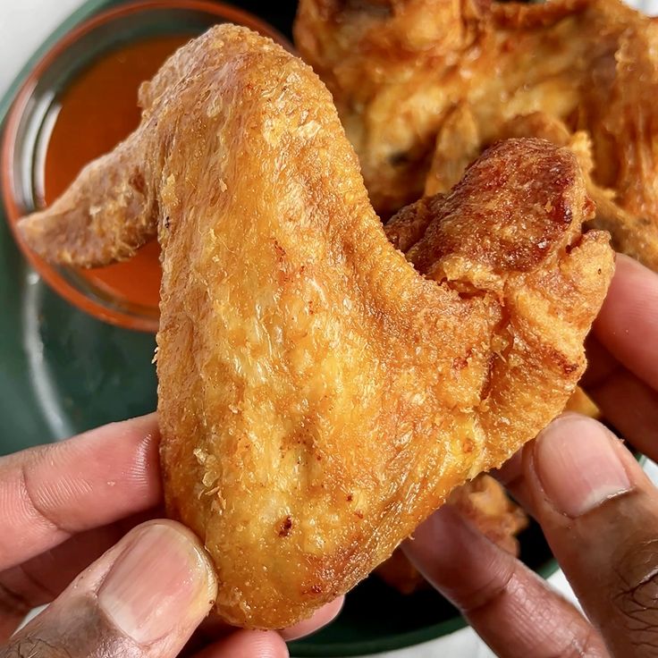 two hands holding fried food in front of a plate with dipping sauce on the side