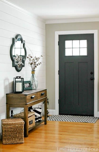 an entryway with a black door and wooden floors in front of a white brick wall