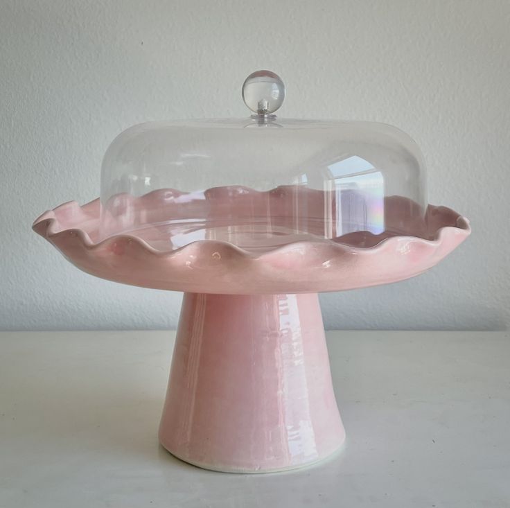 a pink cake stand with a glass dome on top that is covered in frosting