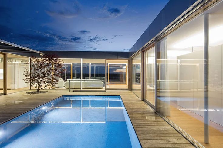 an indoor swimming pool surrounded by glass doors and windows at night with the sky in the background