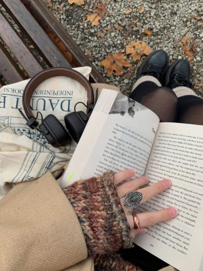 a woman is sitting on a bench reading a book and listening to headphones with her hands