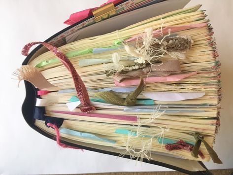 an open book with many different types of paper on it's cover and some ribbons attached to the pages