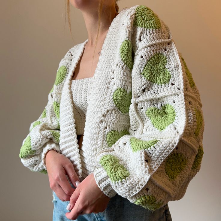 a woman wearing a green and white crochet sweater with leaves on it, standing in front of a wall