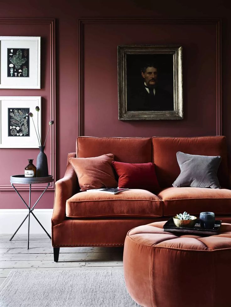 a living room with an orange couch and ottoman in front of a painting on the wall