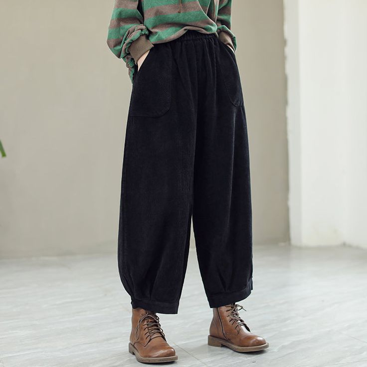 a woman standing in front of a white wall wearing black pants and a green striped shirt