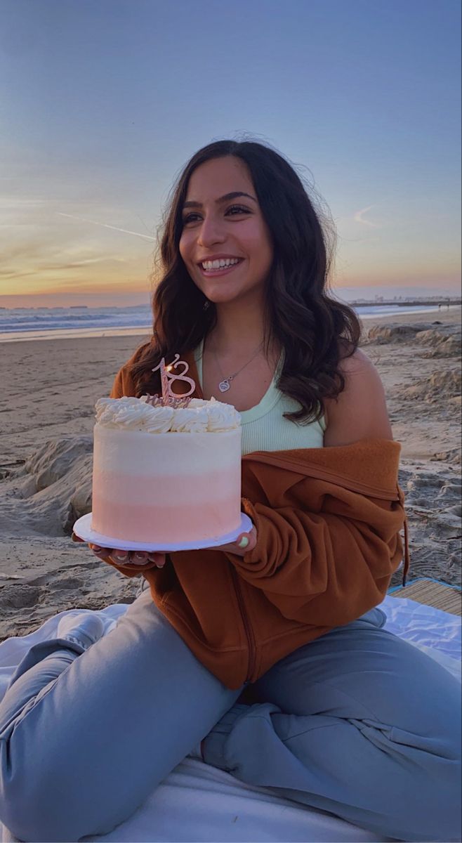 a woman sitting on the beach holding a cake