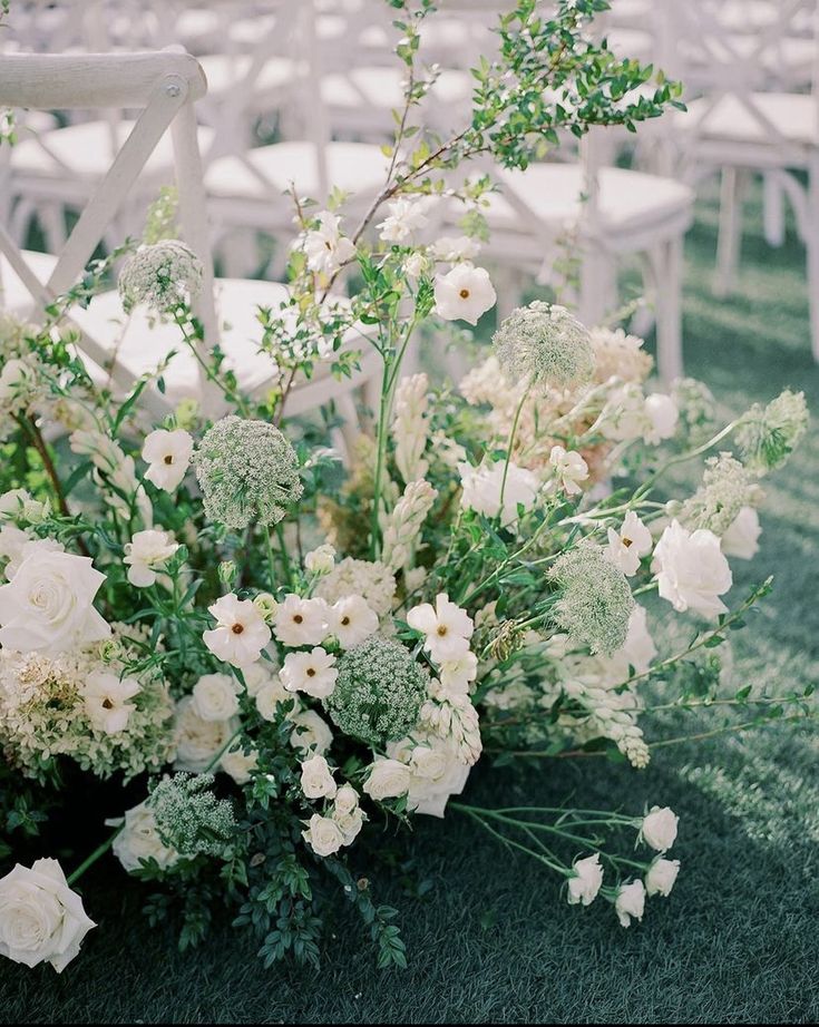 an arrangement of white flowers and greenery in front of rows of chairs at a wedding ceremony