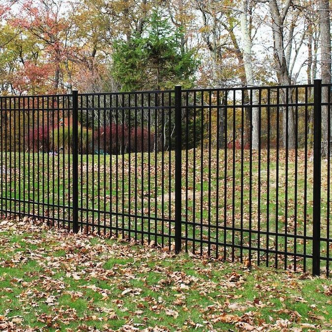 a black iron fence in the middle of a yard with leaves on the ground and trees behind it