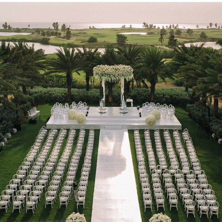 an outdoor ceremony setup with white chairs and floral centerpieces on the lawn, surrounded by palm trees