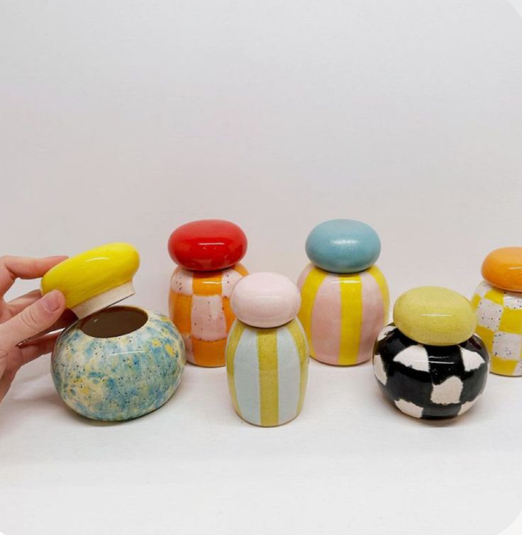 a hand is holding an object in front of several small ceramic objects on a white surface