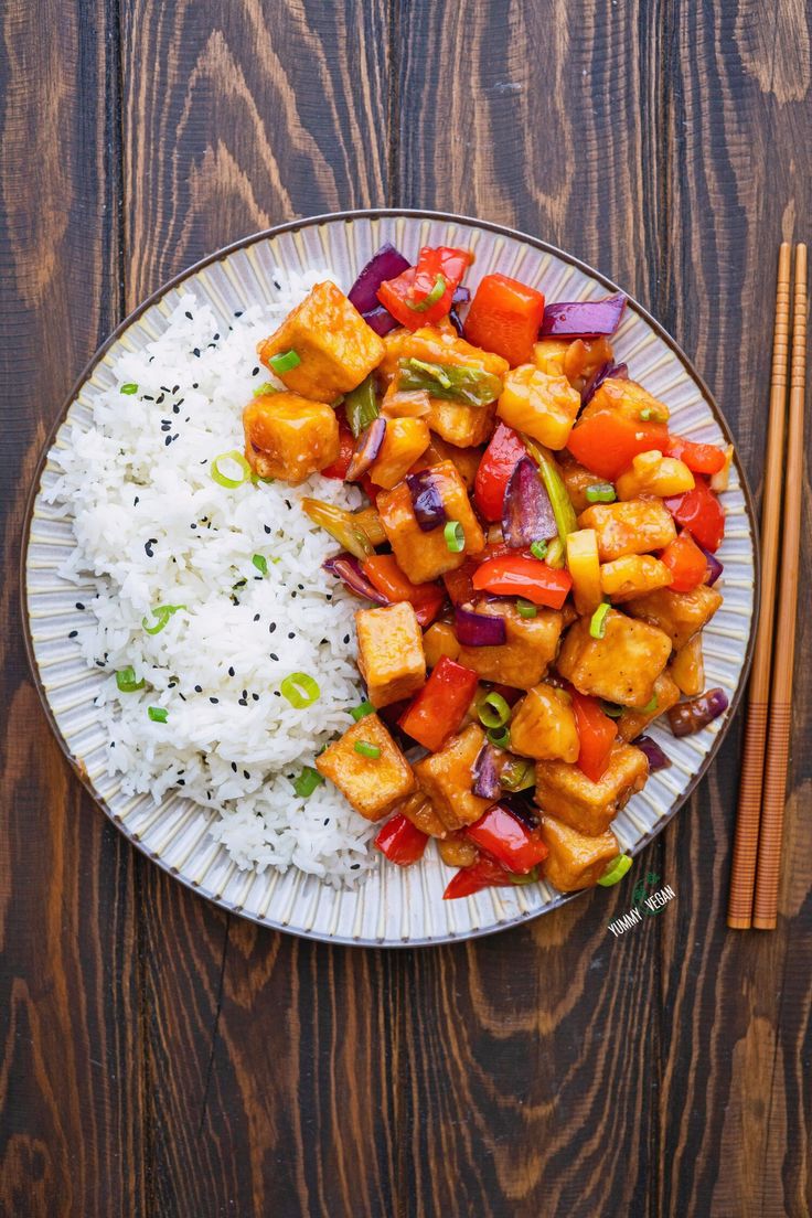 a white plate topped with tofu and rice next to chopsticks on a wooden table