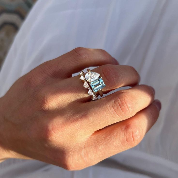 a woman's hand holding a ring with an aqua topazte and diamond center