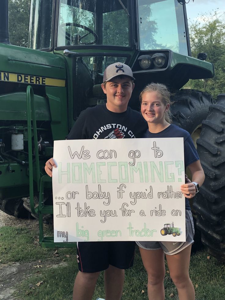 two people standing in front of a tractor holding a sign