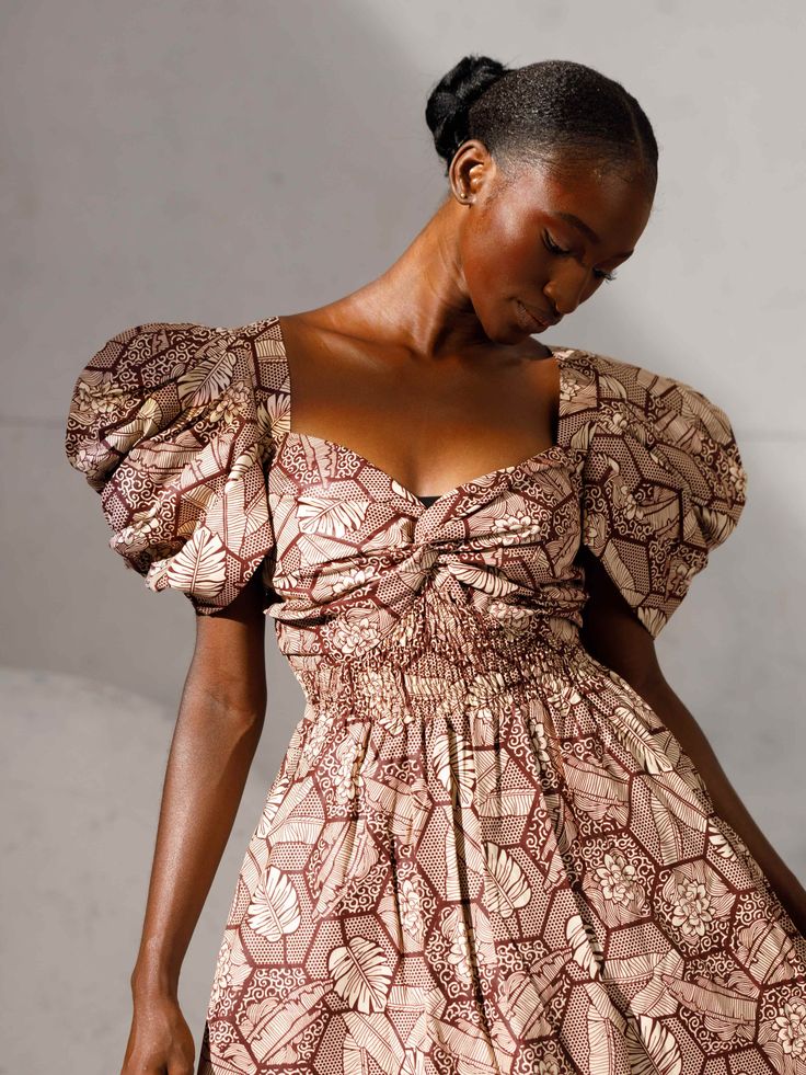 This dress is a testament to our artisans in Nigeria who have meticulously handcrafted fabric sourced from Lagos markets into a garment that transcends fashion and becomes an expression of individuality and a force for good. Exaggerated geometric sleeves Side seam pockets Smocked back bodice Midi Length 100% cotton Wash on cold Hang dry or tumble dry low Pattern placement might vary from pictured. Square Neck Dress With Smocked Bodice For Gatherings, Puff Sleeve Dress With Gathered Neckline For Gatherings, Square Neck Ruched Dresses For Gatherings, Fitted Smock Dress With Puff Sleeves, Square Neck Dress With Gathered Sleeves For Social Gatherings, Square Neck Dress With Gathered Sleeves For Gatherings, Casual Dress With Gathered Sleeves And Square Neck, Chic Smocked Puff Sleeve Dresses, Fitted Midi Dress With Smocked Back For Gatherings