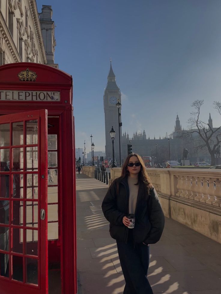 a woman standing next to a red phone booth