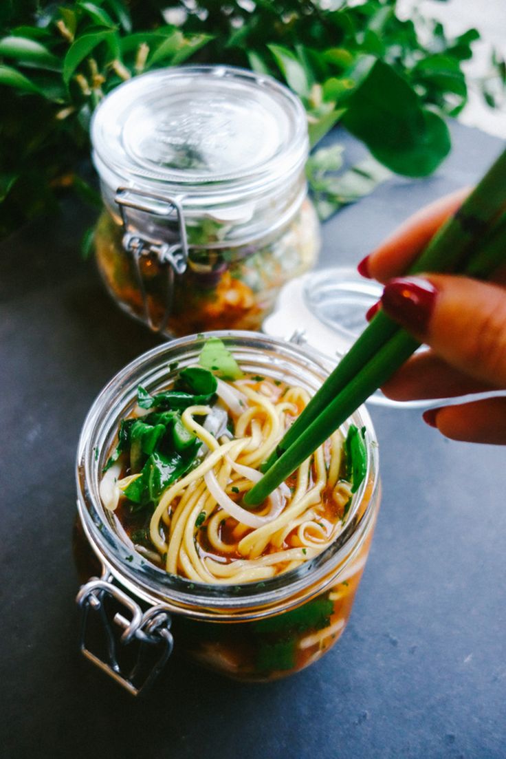 a person is holding chopsticks over a jar of noodles and vegetables on a table