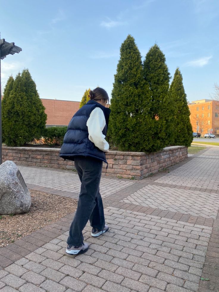 a woman walking down the sidewalk in front of some trees