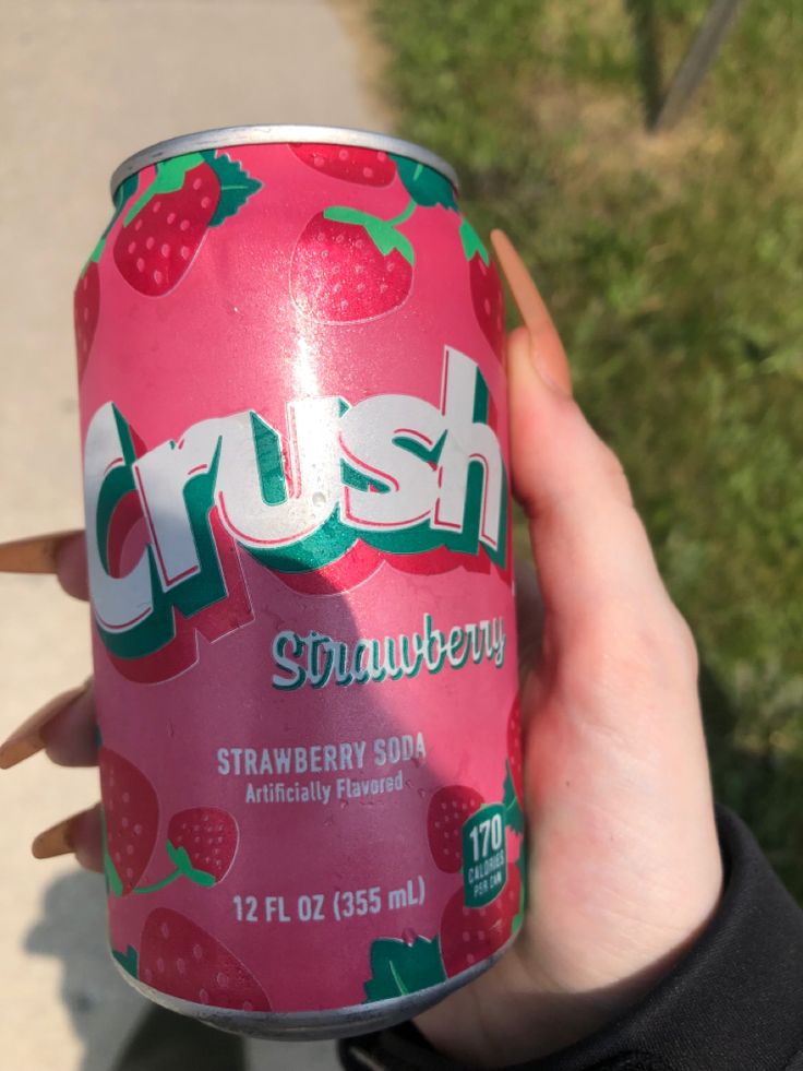 a person holding up a can of crush strawberry soda