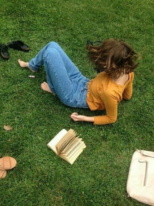 a woman laying on the grass next to some books