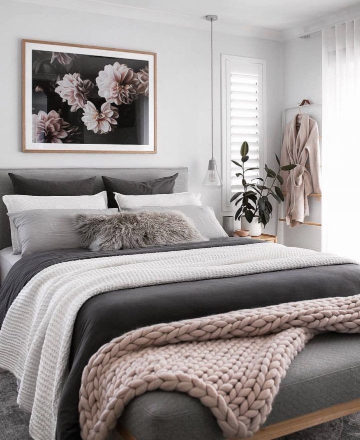 a bedroom with white walls and grey bedding, pink flowers on the window sill