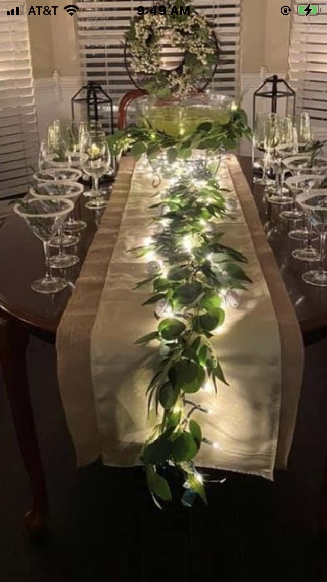 the table is set with wine glasses and greenery on it, along with candles