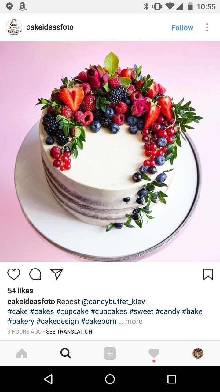 a cake decorated with berries and greenery on top of a white plate, sitting on a pink background