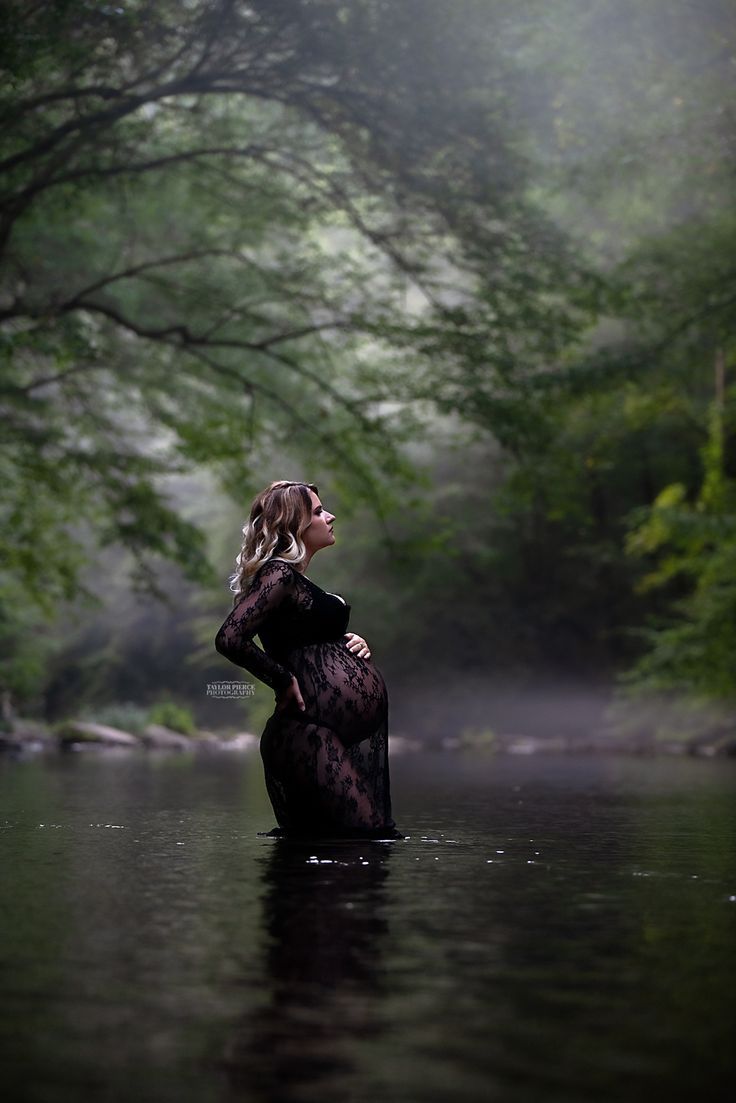 a woman standing in the middle of a body of water surrounded by trees and fog