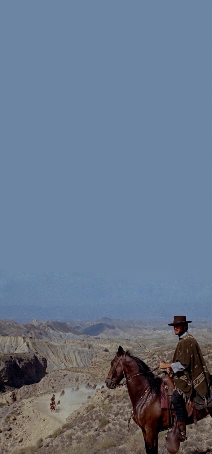 a man riding on the back of a brown horse next to a desert landscape with mountains in the background