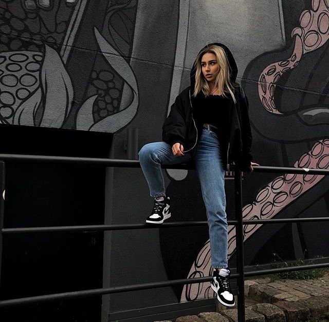 a woman sitting on top of a metal rail next to a wall covered in graffiti