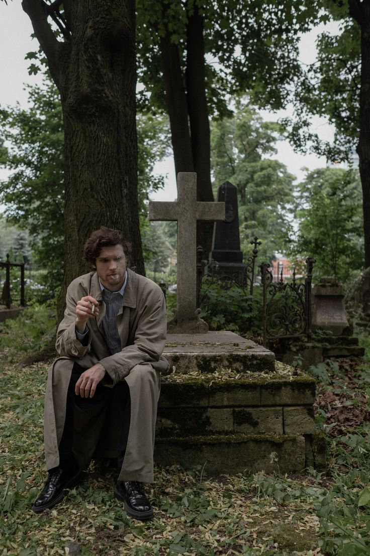 a man sitting in front of a grave on the ground next to a cross and tree