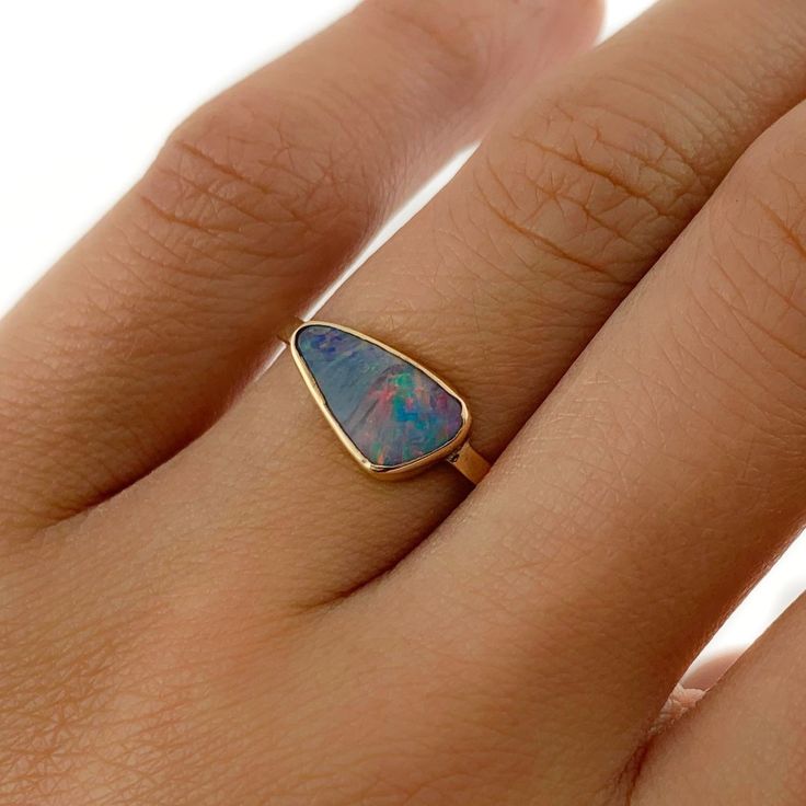 a woman's hand wearing a gold ring with an opal stone