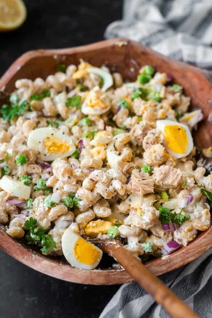 a wooden bowl filled with tuna salad and an egg in the middle on top of a table