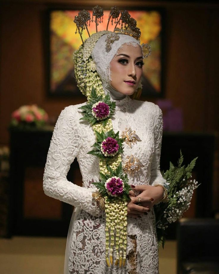 a woman wearing a white dress and headpiece with flowers on her hair, holding a bouquet