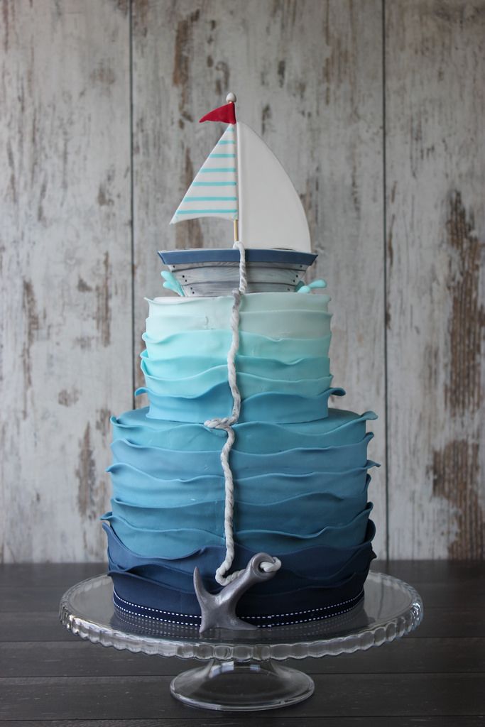 a blue and white cake with a sailboat on top is sitting on a glass plate