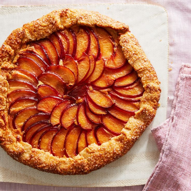 a pie with sliced peaches on top sitting on a white plate next to a pink napkin