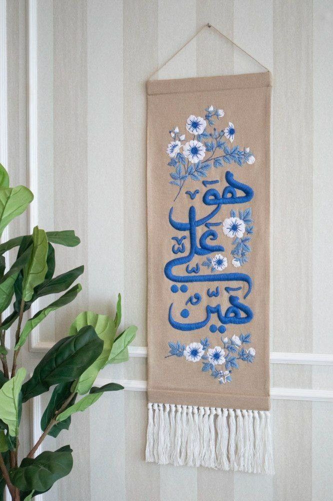 a wall hanging with an arabic calligraphy in blue and white flowers on it next to a potted plant