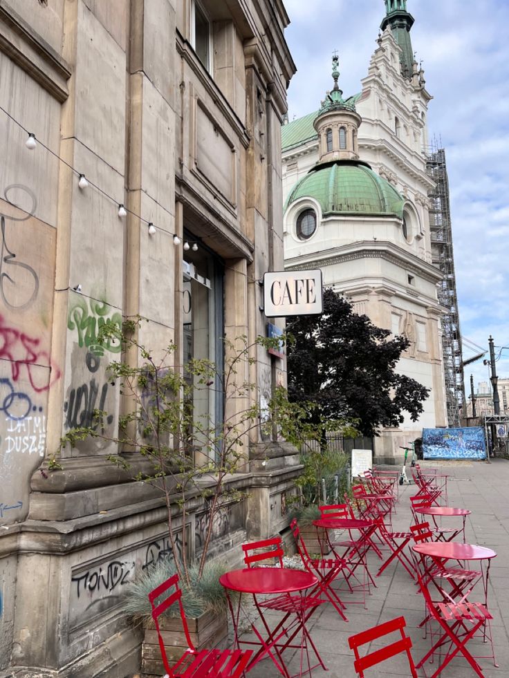 red chairs and tables in front of a building with graffiti on the walls, next to a sign that reads cafe