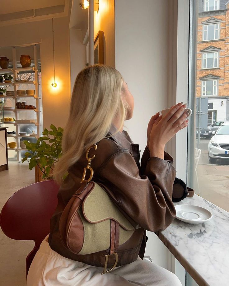 a woman sitting at a table looking out the window with her hand in her purse