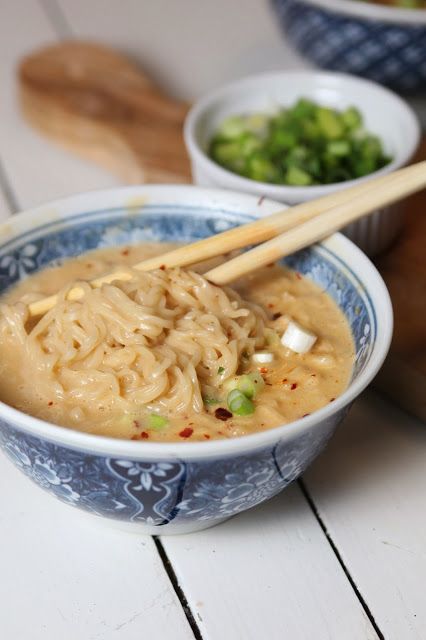 two bowls filled with soup and chopsticks on top of a white wooden table