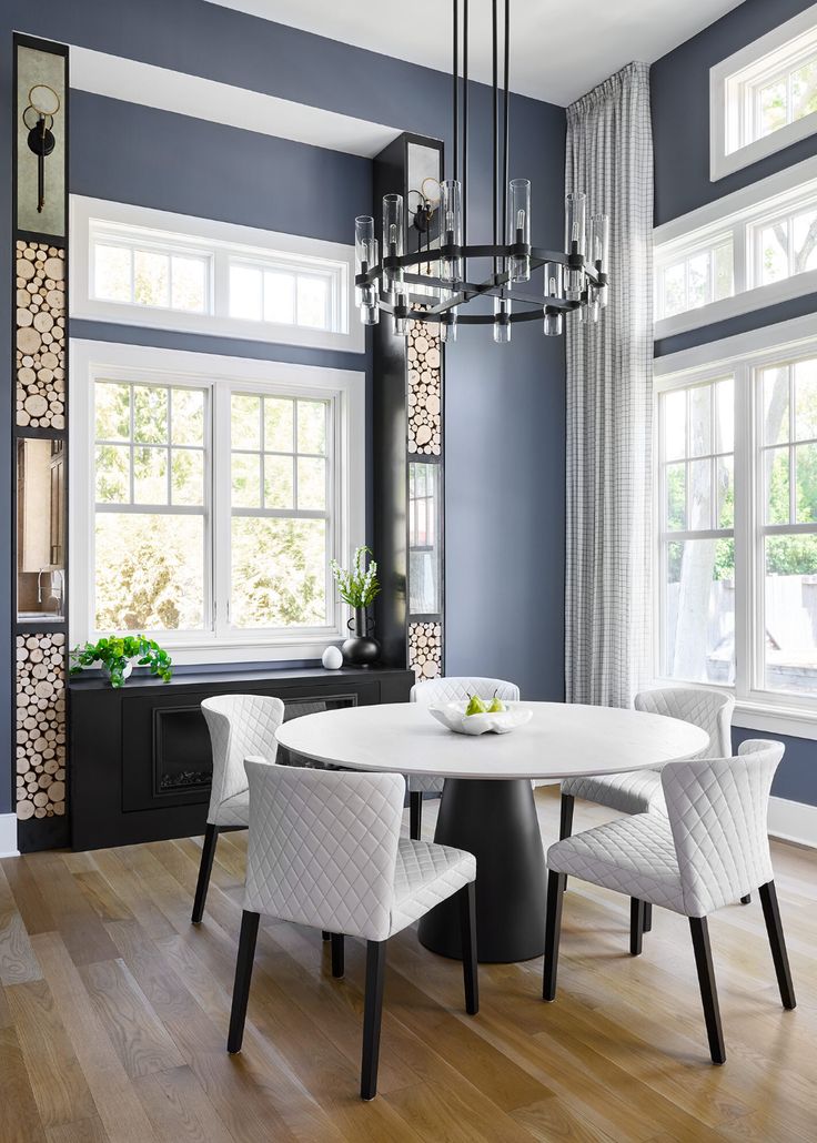 a dining room with blue walls, white chairs and a chandelier hanging from the ceiling