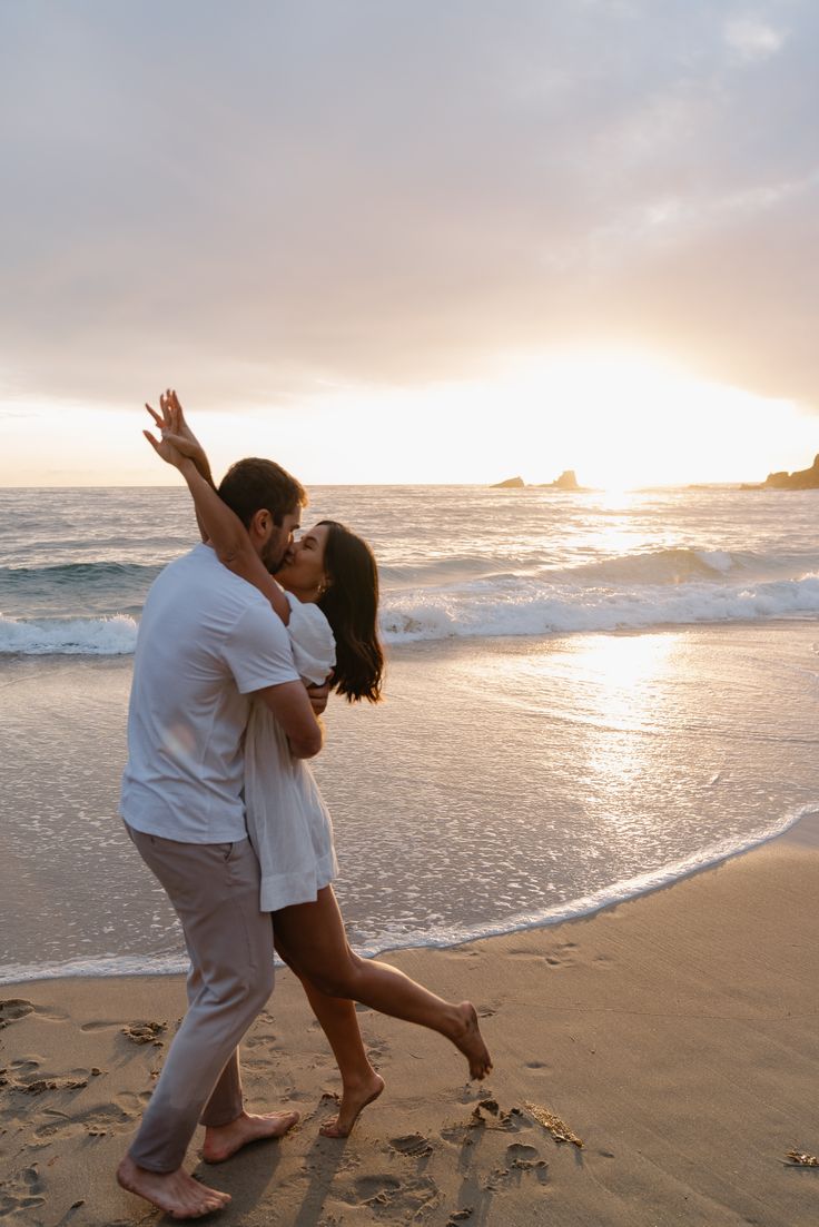 a man and woman hug on the beach as the sun goes down in the background