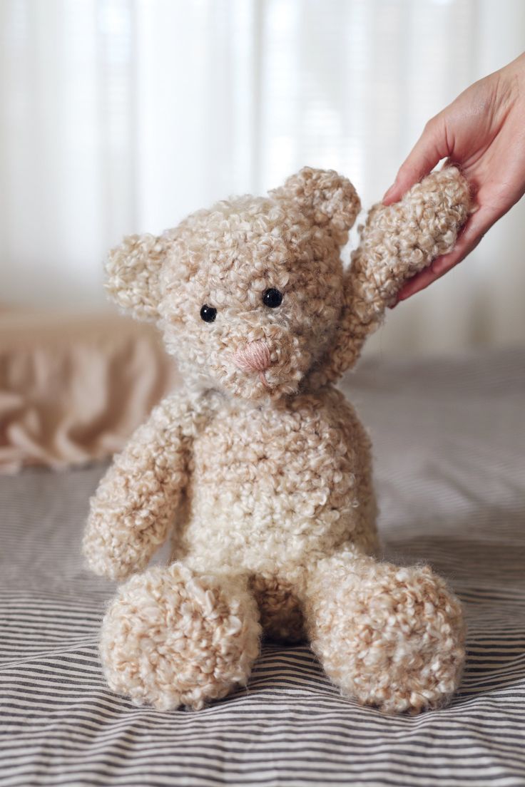 a person is holding the hand of a stuffed teddy bear on top of a bed