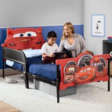 a woman and two children sitting on a bed in a room with disney cars decorations