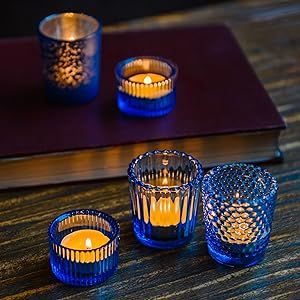 three blue glass candles sitting on top of a wooden table next to a book and pen